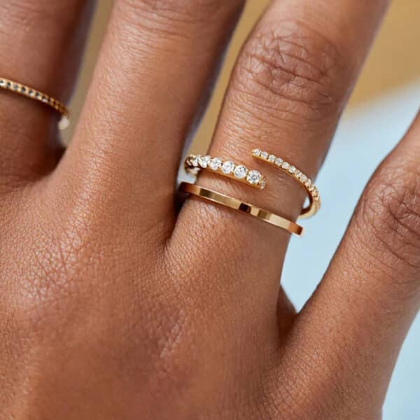 Il s’agit d’une bague réglable et ouverte, plaquée en or, ornée d’oxyde de zirconium. La bague a un design contemporain, avec une bande dorée élégante qui entoure le doigt et qui est ouverte sur le dessus. Une extrémité de la bague est décorée d’une rangée de petites pierres d’oxyde de zirconium qui scintillent et reflètent la lumière, rehaussant la brillance et l’élégance de la bague. La bague est délicate et raffinée, et convient à tous les styles et occasions. Elle peut être portée seule ou associée à d’autres bagues pour créer un effet empilé. Elle est également réglable, ce qui permet de l’adapter à la taille de votre doigt. La bague est plaquée en or, ce qui signifie qu’elle est recouverte d’une fine couche d’or. Le plaquage en or donne à la bague une apparence luxueuse et une couleur chaude, tout en la rendant plus accessible et plus légère. L’oxyde de zirconium est pierre de synthèse à l’éclat éblouissant.